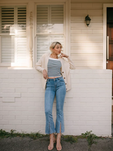 a lady wears a striped top with a beige cardigan and flared jeans